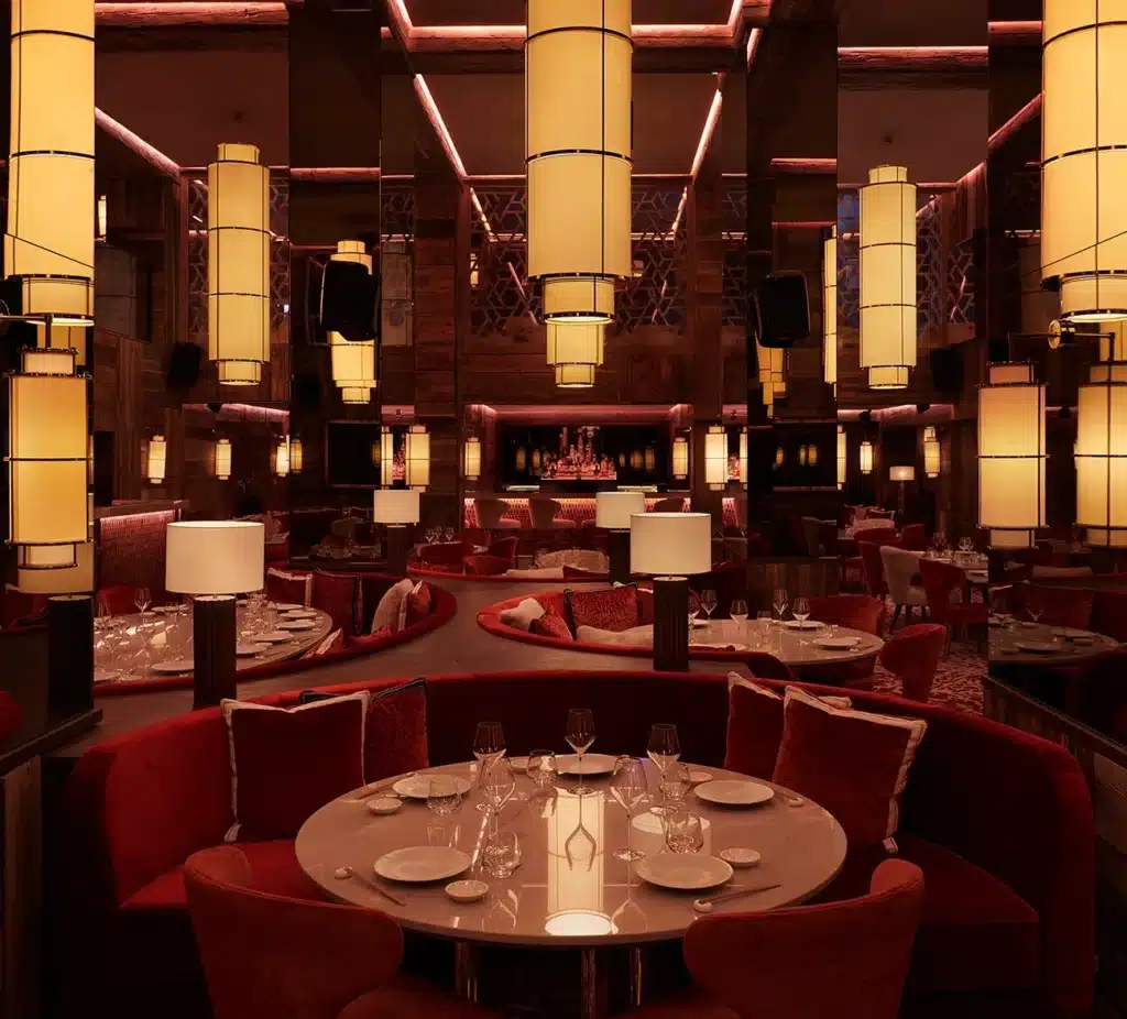 Dining room at Kinugawa Courchevel with red velvet booths, round tables and large hanging lanterns.